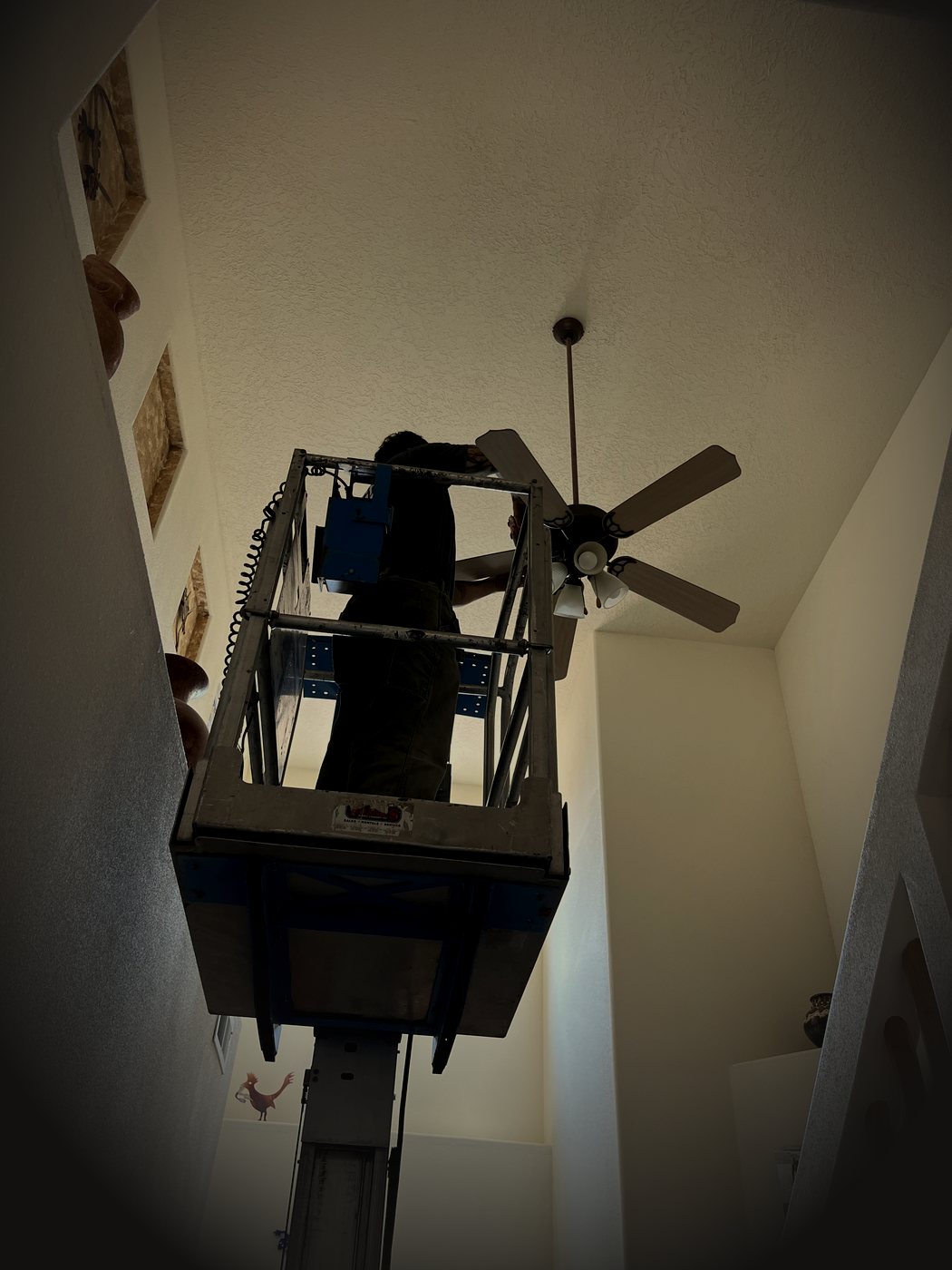 Ethan of Duke City Lift & Fix on a scissor lift replacing a ceiling fan in a two-story Albuquerque stairwell
