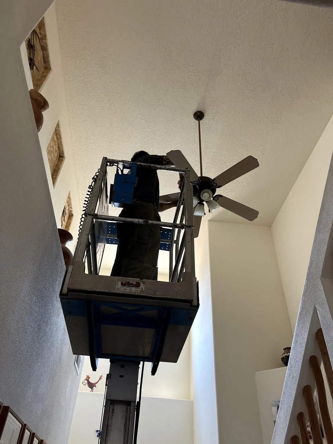 Ethan replacing a ceiling fan from a scissor lift in a two-story stairwell