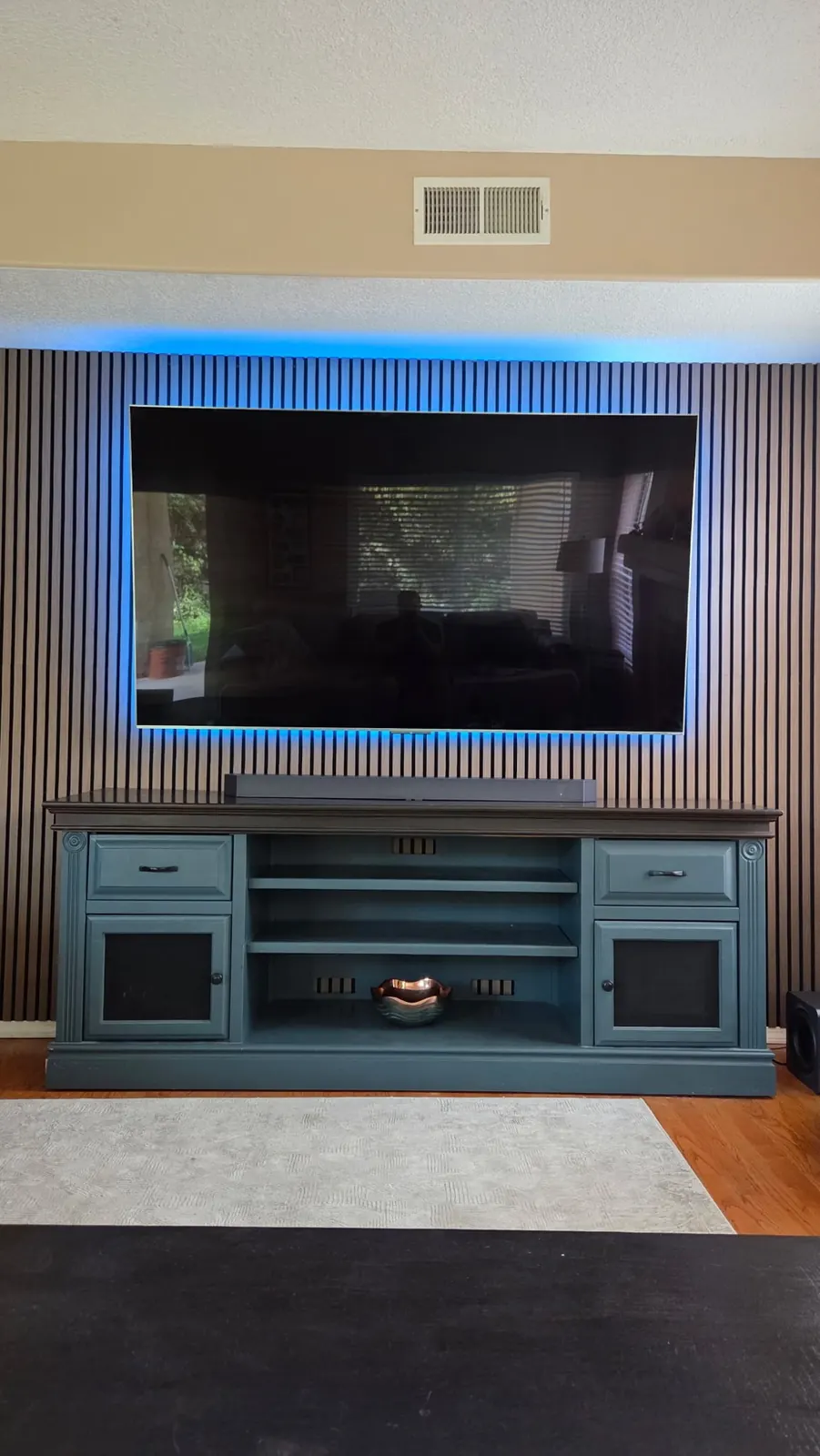 Large TV centered on a slat wall above a media console, wires hidden